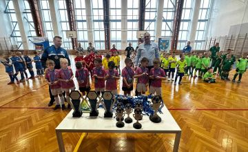 Stojące na boisku dzieci a przed nimi medale oraz trofea